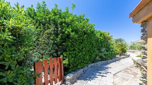 Un sentiero in pietra che si snoda attraverso un fitto arbusto verde, con una recinzione in legno su un lato e un edificio sull'altro.