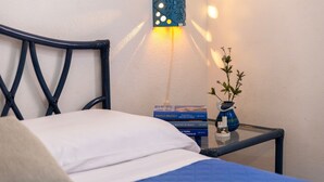 Un letto con testiera, un comodino con un vaso e libri, e una lampada fissata al muro.