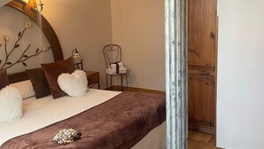 Een slaapkamer met een bed, nachtkastje, stoel, houten garderobe en decoratieve wandversiering.
