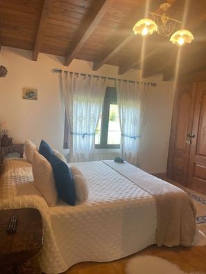 A bedroom with a bed, curtains, a wooden ceiling, a nightstand, and a door. - Room 'Doble Jazmín' with Mountain View, Shared Terrace and Wi-Fi (Rubayo)