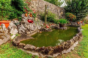 A garden with a pond, stone walls, and potted plants.
