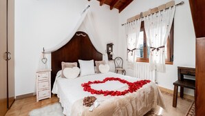Ein Schlafzimmer mit Himmelsbett, Nachttisch, Stuhl, einem Fenster mit Vorhängen und Holzboden.