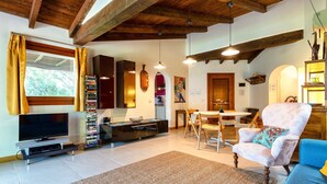 A living room with a TV, bookshelf, dining area, and a patterned armchair. - Holiday Home 'Medit' with Private Terrace, Wi-Fi and Air Conditioning (Stintino)