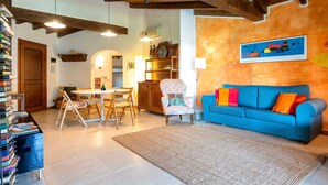 A living room with a blue sofa, a dining table with chairs, a wooden cabinet, and a painting on the wall. - Holiday Home 'Medit' with Private Terrace, Wi-Fi and Air Conditioning (Stintino)