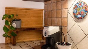 Eine Kaffeemaschine, ein Topf mit Pflanze, ein Mülleimer und ein Wandbehang in einer Küche.