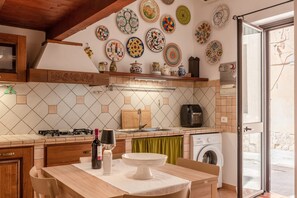 A kitchen with a dining table, a sink, a stove, a washing machine, and a variety of decorative plates on the wall.