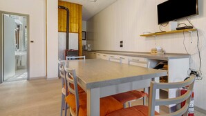 A modern kitchen with a wooden accent wall, a dining area with a table and chairs, and a mounted television. - Apartment 'Berthold' with Mountain View, Shared Terrace and Wi-Fi (Ledro)