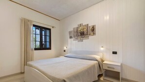 A bedroom with a bed, bedside tables, a window with curtains, and wall-mounted artwork. - Apartment 'Berthold' with Mountain View, Shared Terrace and Wi-Fi (Ledro)