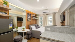 A compact living space with a kitchenette, a dining area, a sofa, and a TV. - Great Holiday Vacation: 1BR Condo w/ 2 Queen Beds (Quezon City)