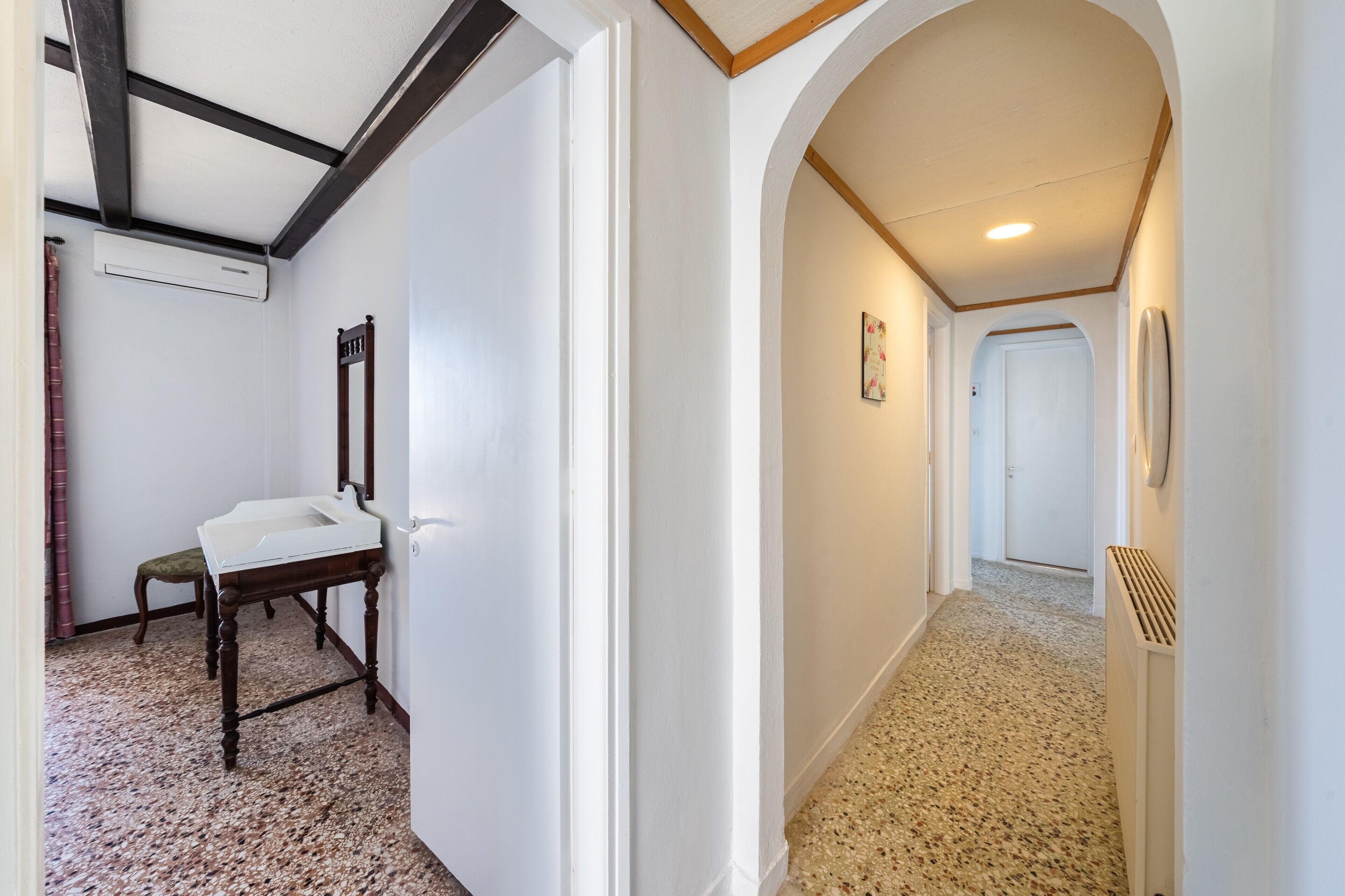 A hallway with a white wall, a wooden bench, a white sink, and a radiator.