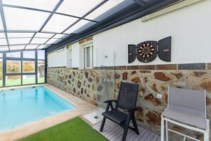 An indoor swimming pool with a glass ceiling, stone wall, and a dartboard.