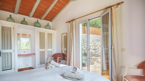 A bedroom with a bed, two chairs, a window, and a sliding glass door leading to an outdoor area. - Can Miquel: Charm and Pool in Pollença (Pollensa)
