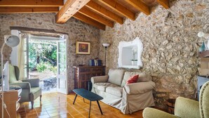 A stone-walled room with a wooden ceiling, a sofa, a chair, a small table, and a desk with a lamp. - Can Miquel: Charm and Pool in Pollença (Pollensa)