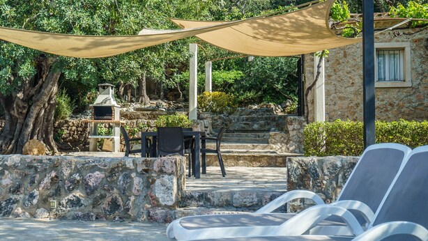A stone patio with lounge chairs, a table, and a barbecue grill. - Can Miquel: Charm and Pool in Pollença (Pollensa)