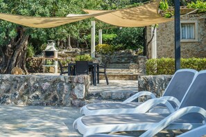 Een terras van natuursteen met loungestoelen, een tafel en een barbecue.