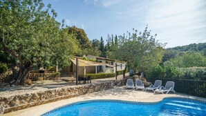 A swimming pool with lounge chairs, a stone house with a patio, and surrounding greenery. - Can Miquel: Charm and Pool in Pollença (Pollensa)
