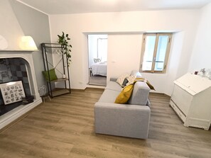 A modern living room with a grey sofa, a fireplace, a plant, and a view into another room.