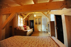 Une pièce confortable avec un lit, un canapé, un plafond en bois et une porte donnant sur une autre pièce.