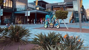 A modern building with a 'Hola!' sign, a 'lefties' store, and a large colorful sculpture in the plaza. - Vacation 'Pura Vida' with Sea View, Shared Pool and Wi-Fi (Puerto Rico de Gran Canaria)