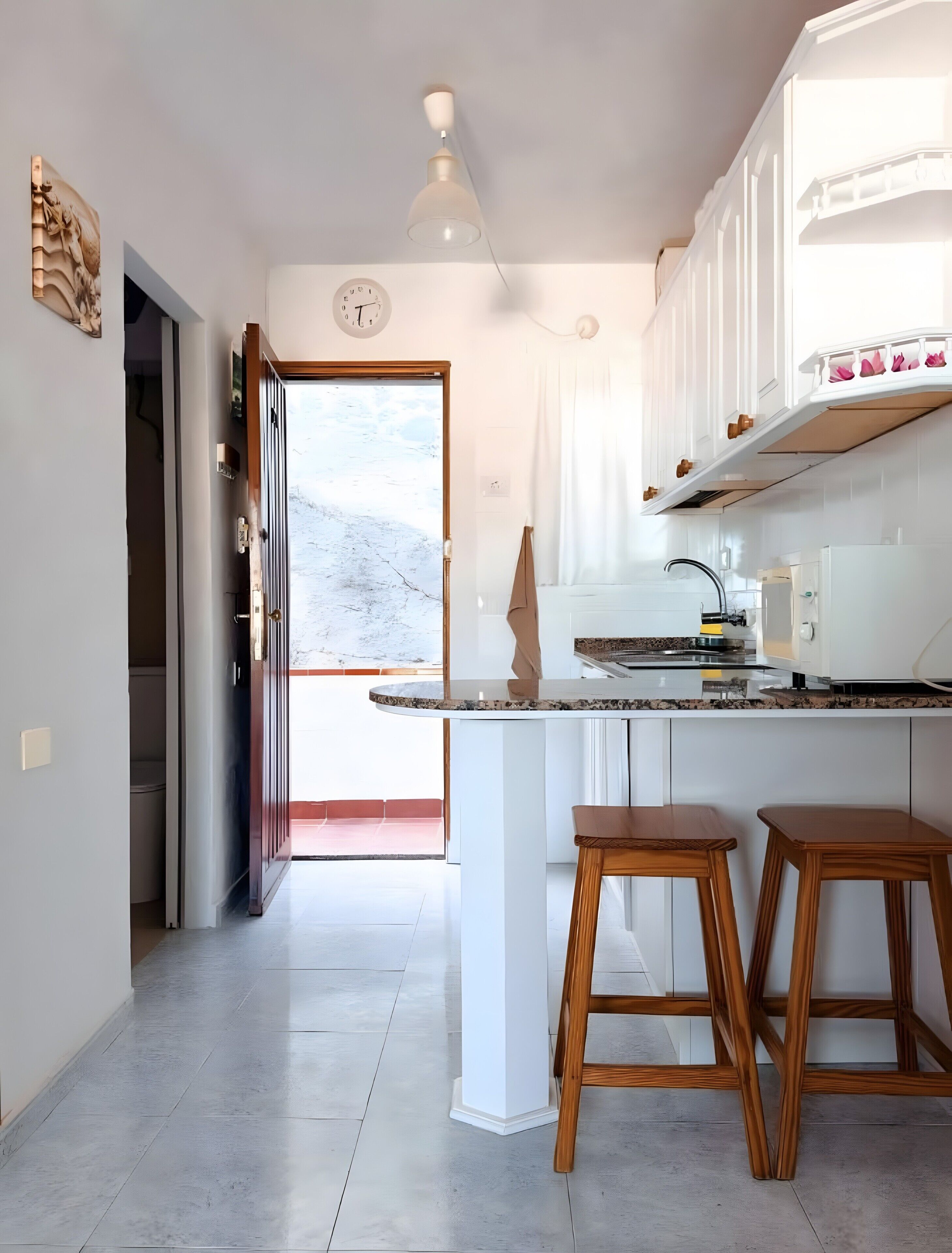 A kitchen with a marble countertop, wooden stools, a ceiling fan, and a view to the outside.