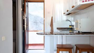 A kitchen with a marble countertop, wooden stools, a ceiling fan, and a view to the outside.