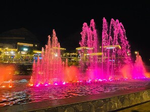 A nighttime fountain with multiple water jets illuminated in pink and orange.