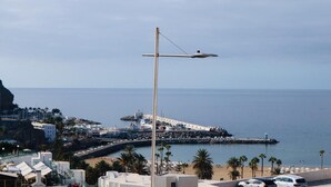 A coastal cityscape with a prominent street lamp, a pier, and a beach area. - Vacation 'Pura Vida' with Sea View, Shared Pool and Wi-Fi (Puerto Rico de Gran Canaria)