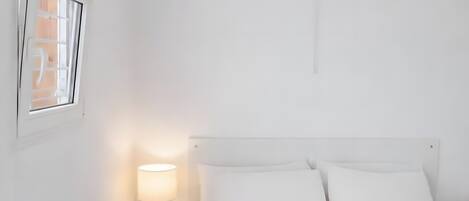 A minimalist hotel room with a bed, bedside lamp, and a hanging light fixture.