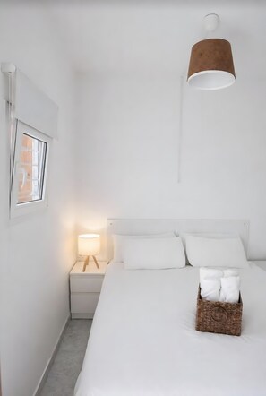 Habitación de hotel minimalista con cama, lámpara de noche y una lámpara colgante.
