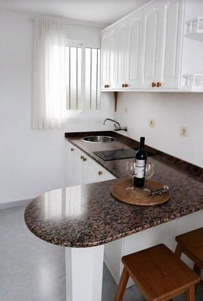 Una cocina con armarios blancos, encimera de granito, pileta de acero inoxidable y una botella de vino sobre la encimera.