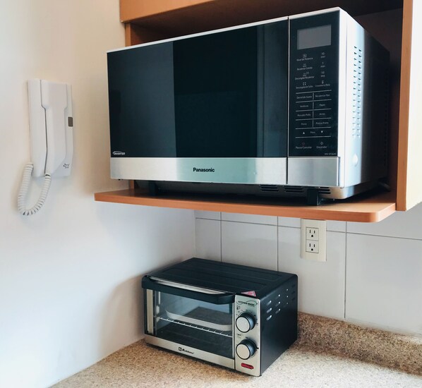 A kitchen with a microwave oven on a shelf and a toaster oven on the countertop.