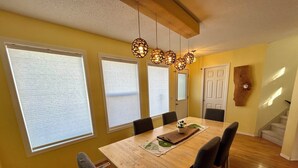 Un coin repas avec une table en bois, six chaises et un luminaire suspendu au plafond.