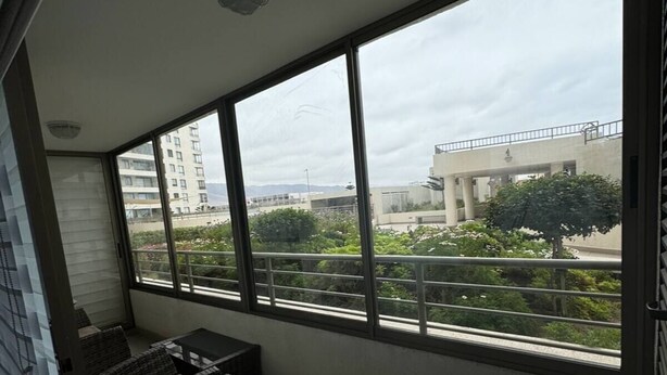 A balcony with wicker furniture and a view of a building and greenery.