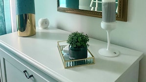 Une commode blanche avec un miroir, deux lampes, une petite plante en pot et un plateau décoratif.