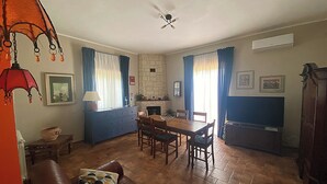 Un salon avec un canapé en cuir marron, une table à manger en bois avec des chaises, une cheminée et un ventilateur de plafond.