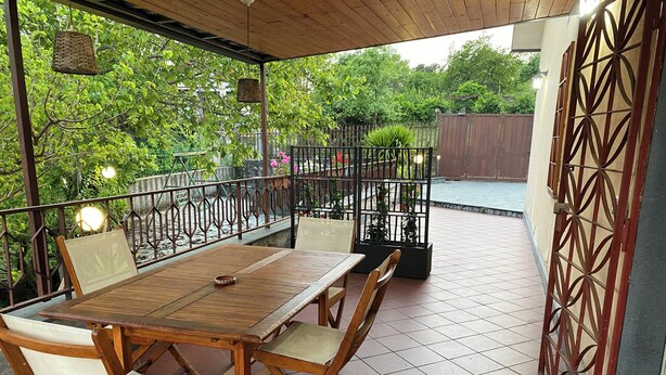 Une table et des chaises en bois sur une terrasse, avec vue sur un jardin et une piscine.
