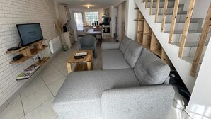 A modern living room with a grey sectional sofa, wooden shelves, a flat-screen TV, and a staircase with wooden steps.