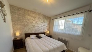 A bedroom with a bed, two bedside tables with lamps, a window with curtains, and a radiator.