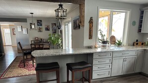 Una cocina con encimera de mármol, taburetes de madera y una zona de comedor con alfombra roja.