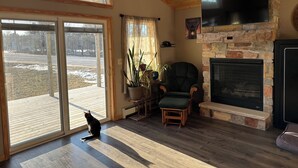 Una sala de estar acogedora con chimenea, un sillón cómodo y un gato sentado junto a la puerta.