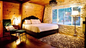 A wooden cabin bedroom with a bed, a chair, a lamp, and a window. - Big Bear Getaway w/ Hot Tub, King Bed & Private Yard (Big Bear)