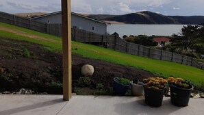 A view of a house with a wooden deck, a fenced yard, and a body of water in the background.