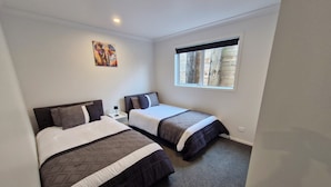 A bedroom with two beds, a nightstand, a window, and a painting on the wall.