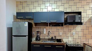 Een kleine keuken met een koelkast, magnetron, fornuis en spoelbak.
