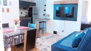 Un espace de vie compact comprenant un coin repas, une cuisine et un téléviseur fixé au mur.