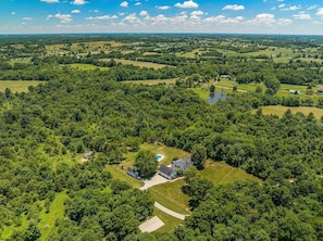 An aerial view of a rural landscape with a large house surrounded by dense trees and open fields.