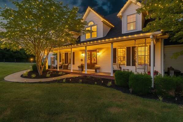 Une maison à deux étages dotée d’un porche couvert, d’un jardin aménagé et de guirlandes lumineuses.
