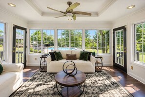 Une véranda avec un canapé blanc, une table basse ronde et un ventilateur de plafond.