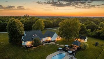 A large house with a swimming pool, surrounded by a well-maintained lawn and trees.