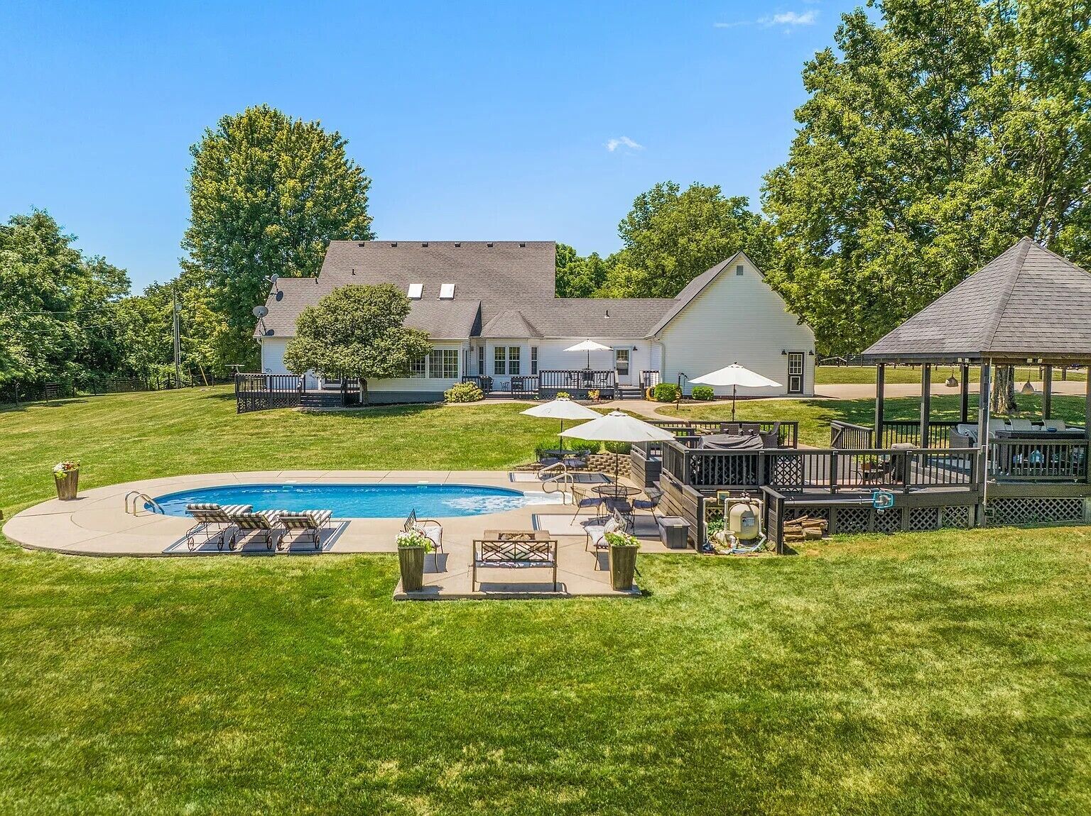 Une grande maison avec une piscine, du mobilier d’extérieur et un belvédère.